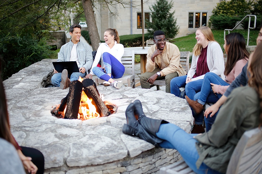 A group of IU Bloomington students sitting around an outside fire pit, talking and laughing. 